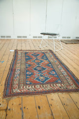 Angled view of hand-knotted Caucasian rug, showing geometric madder red, sky blue medallions, intact selvage, and fringe.