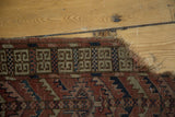 Dog-eared corner of antique Turkmen rug, geometric square border, tattered fringe.