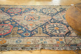 Antique Soumac carpet: geometric blush and navy diamond medallion, wave border, and tattered edge.