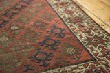 Close-up detail of hand-knotted antique Belouch rug: navy medallions on chestnut field, starburst border.