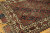 Antique Belouch rug's geometric starburst border in antique ivory, showing worn pile and tattered end.