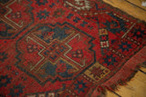 Tattered edge and worn cherry red pile of a vintage Beshir rug with navy gul motif.