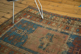 Antique Kazak rug close-up: madder red and sky blue geometric patterns, age-softened wear, tattered edge.