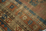 Antique Kazak rug's madder red starbursts and 'running T' border, revealing worn foundation.
