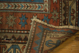 Close-up of antique Kazak rug showing hand-knotted foundation, geometric starbursts, and tattered fringe.