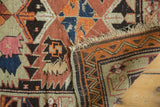 Dog-eared corner of antique Caucasian rug, tattered fringe, geometric tangerine, charcoal, and blue pattern.