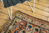 Corner of antique Caucasian rug, rectilinear patterns, tangerine, navy, beige, tattered fringe.