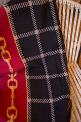 Equestrian blanket fold with red horse bit chain and dark plaid design.