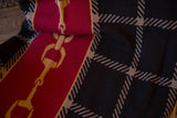 Knitted golden horse bit chain on a red stripe and dark plaid blanket.
