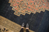 Feet on antique Persian Doroksh rug, highlighting navy field wear, blush stepped contour, and beige lily border.