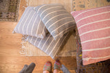 Stacked hand-woven gray cotton pillows with white stripes and decorative ties.