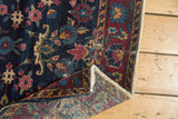 Vintage Yezd rug's folded corner, highlighting indigo floral design, red border, and tattered side.