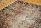 Worn brick red Lilihan rug corner, with scrolling vinery, navy blue, and visible foundation.