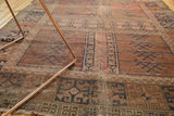 Antique Turkmen rug close-up: faded blush and navy geometric patterns, with visible exposed foundation.
