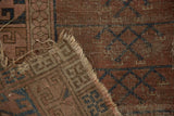 Antique Turkmen rug close-up: faded blush pile, geometric navy design, exposed foundation, tattered edge.