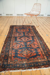 Vintage Hamadan rug corner with geometric patterns, navy border, and tattered ivory fringe.