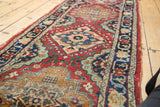 Vintage Tabriz runner's intricate navy medallion, cherry red field, floral patterns, and worn side tatter.