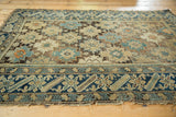 Angled view of an antique Caucasian rug showing geometric starbursts, blue borders, and aged edges.