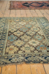 Visible split and tattered fringe on the dark blue geometric border of an antique Caucasian rug.