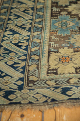 Antique Caucasian rug: geometric borders, stylized patterns, blue, brown, ivory tones, worn fringe.