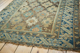 Corner of antique Caucasian rug with geometric blue border, starburst field, and tattered edges.