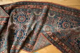 Folded vintage Lilihan rug with geometric patterns in dusty rose, indigo, and teal.
