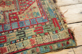 Detail of vintage Caucasian rug corner: geometric stylized flowers, visible knot heads, and frayed edges.