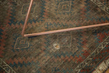 Vintage Belouch rug close-up showing a hole amidst worn geometric madder red and blue patterns.