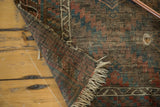 Folded vintage Belouch rug revealing its foundation through a hole and tattered fringe.