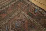 Etched brown and blush geometric gul motifs on an antique hand-knotted Belouch rug.