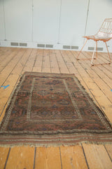 Angled view of antique Persian Belouch rug, geometric gul motifs, mellowed colors, and frayed ends.