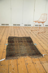 Close-up of antique Belouch rug's patterned field, with worn barber pole borders and tattered fringe.