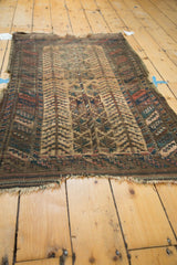 Antique Persian Belouch rug's worn end, revealing barber pole borders and plant of life motif.