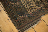 Antique Belouch rug corner, detailing tattered fringe and barber pole border with visible knot heads.