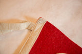 Pointed tip of vintage red felt pennant, with cream border, tie, and small pinhole detail.