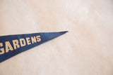 Vintage dark blue felt pennant close-up, showing tan 'GARDENS' lettering and pointed tip.