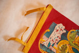 Top corner of vintage Yellowstone felt flag showing red felt, yellow binding, ties, and Old Faithful detail.