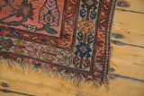 Antique Malayer rug corner, featuring tattered fringe and a faded brick red and blue border.