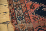 Tattered edge of an antique Malayer rug, showing faded brick red, navy blue, and ivory border patterns.