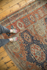 Feet on an antique Caucasian Soumac rug, revealing madder red and navy geometric patterns with authentic wear.