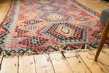 Aged Turkish Kilim carpet showing red and blue diamond motifs and a time-worn end.