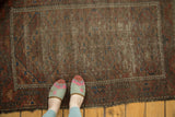 Antique Belouch rug's worn pile texture with faded madder red, apricot, and navy geometric patterns.