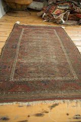 Worn corner of an antique Belouch rug with madder red, chestnut, and navy concentric patterns, tattered.