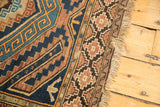 Vintage Caucasian rug's running T borders and geometric patterns in navy, copper, and beige with fringe.