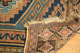 Dog-eared corner of Vintage Caucasian rug, showing worn fringe, intact selvage, geometric pattern.