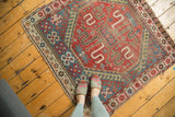 Corner of vintage Caucasian rug showing geometric pinwheel pattern and tattered fringe.