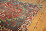 Hard tatter and loss on corner of vintage Caucasian rug, showing geometric red and blue motifs.
