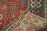 Folded vintage Caucasian rug, worn red, blue geometric pile, exposed foundation, frayed fringe.