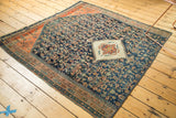 Corner of antique Persian rug fragment featuring navy Herati field, terra cotta abrashes, and teal border.