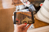 Vintage Kilim rug wallet with earthy geometric patterns and black faux leather trim, held in hand.